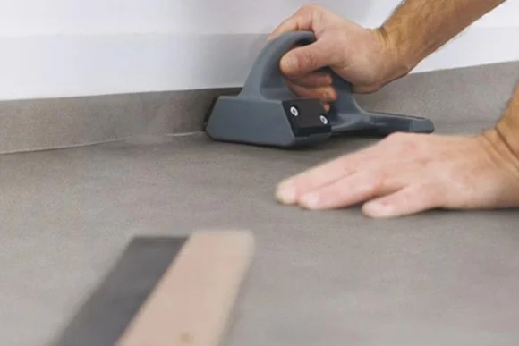 Hand schneidet Bodenbelag mit Cutter